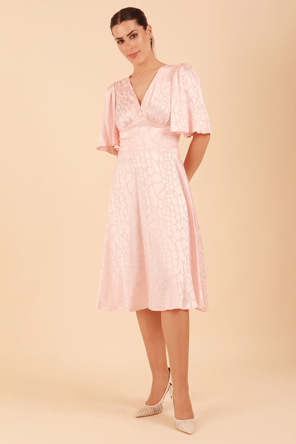 model wearing diva catwalk cambrian satin swing dress with bell short sleeve wide asymmetric waistband and pleating under bust in pink front