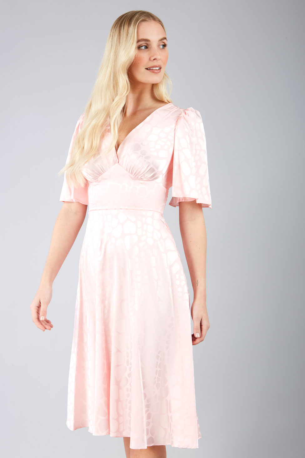 model wearing diva catwalk cambrian satin swing dress with bell short sleeve wide asymmetric waistband and pleating under bust in pink front