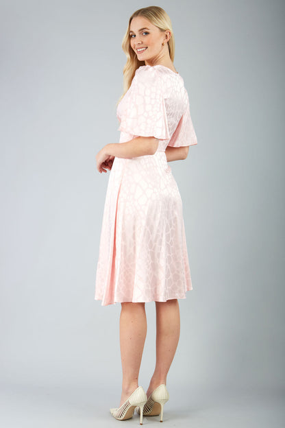 model wearing diva catwalk cambrian satin swing dress with bell short sleeve wide asymmetric waistband and pleating under bust in pink front
