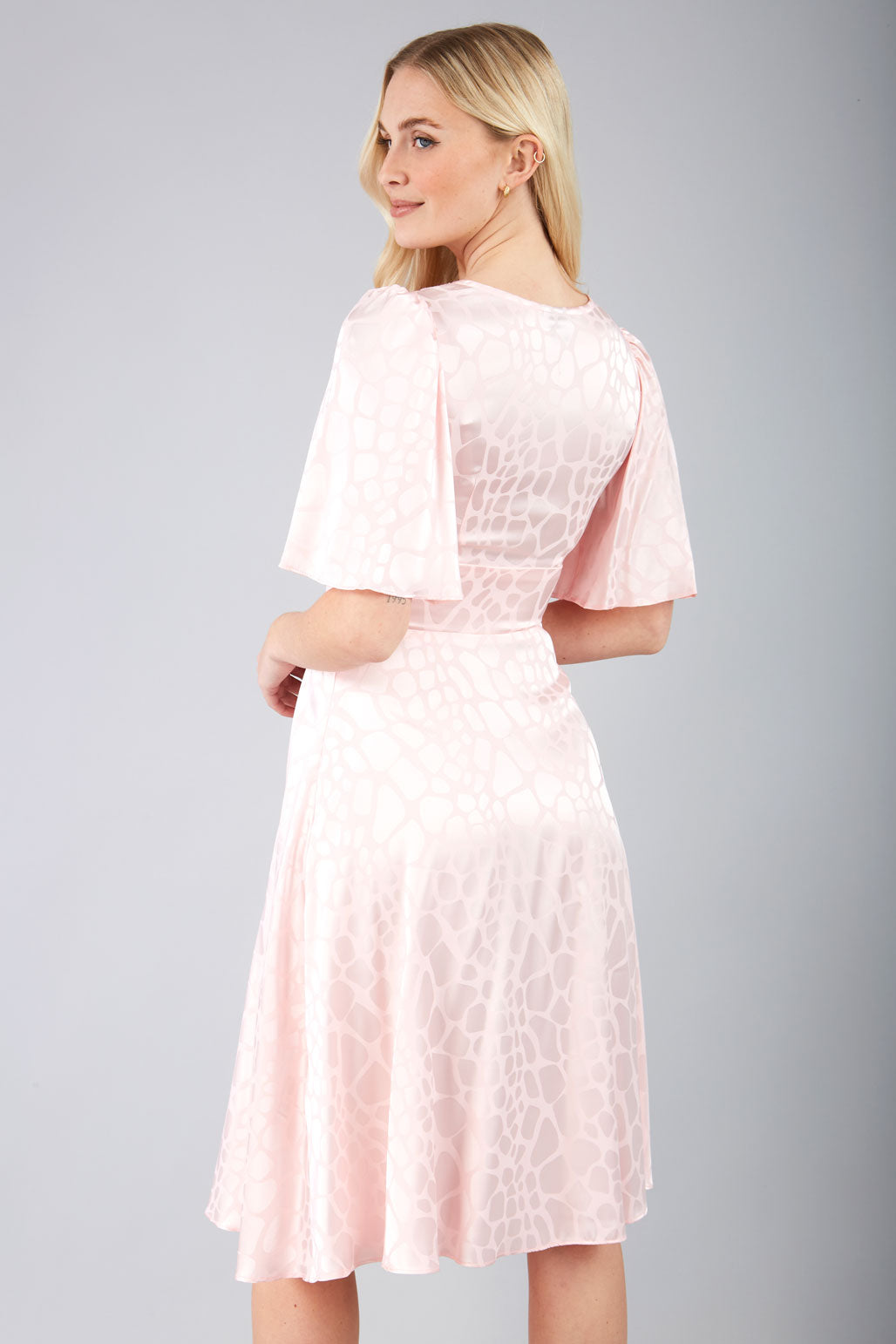 model wearing diva catwalk cambrian satin swing dress with bell short sleeve wide asymmetric waistband and pleating under bust in pink front
