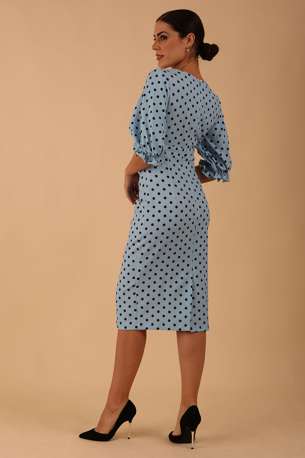Blonde model wearing Diva Catwalk Palacio Pencil dress v neckline and pleating across the tummy with puffed short sleeves in blue polka dot front