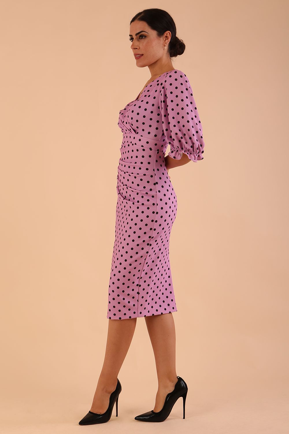 brunette model wearing diva catwalk palacio pencil fitted dress with three quarter puffed sleeve and pleating across the body with overlapping v-neckline in pink polka dot front