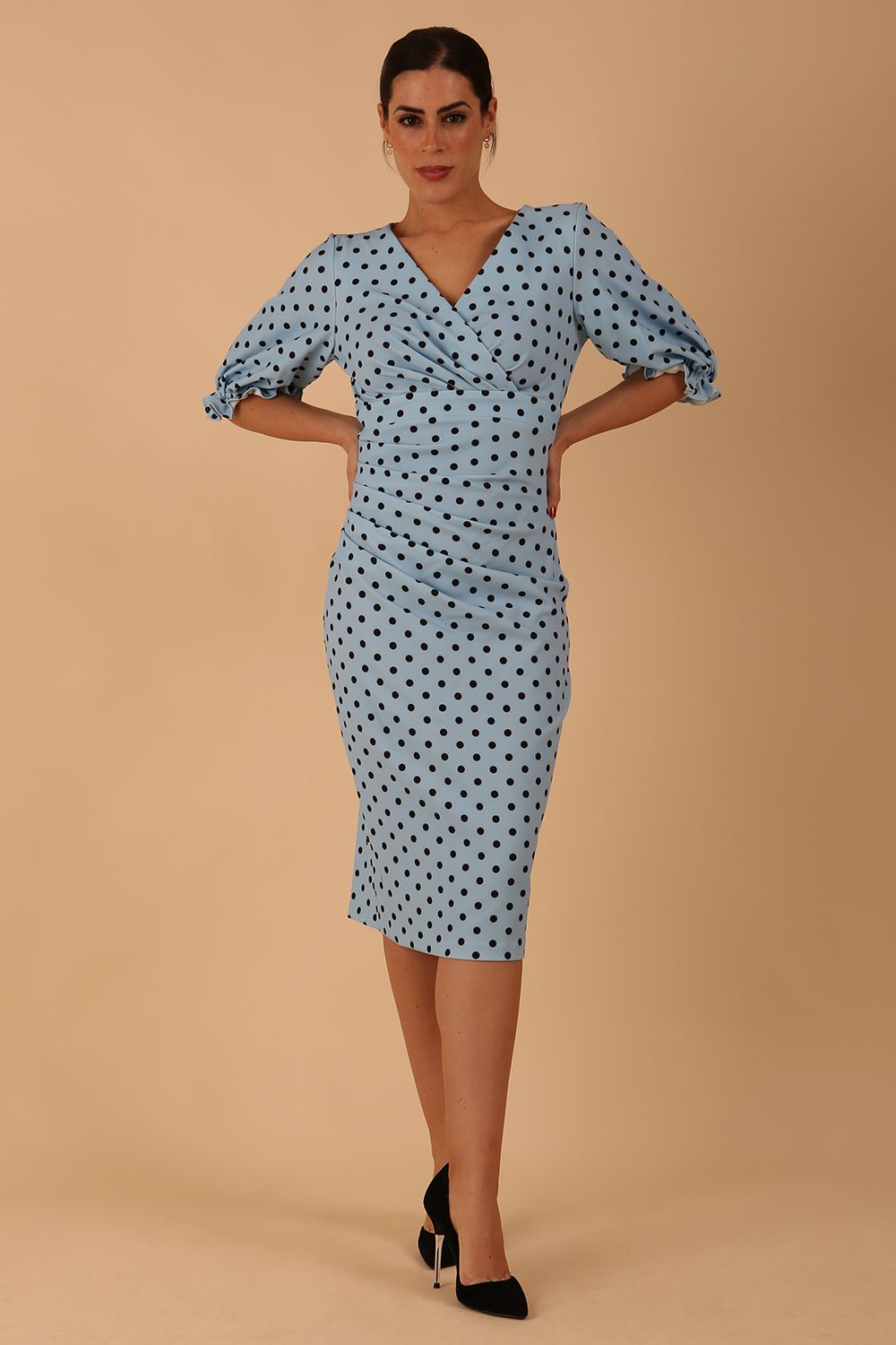 Blonde model wearing Diva Catwalk Palacio Pencil dress v neckline and pleating across the tummy with puffed short sleeves in blue polka dot front