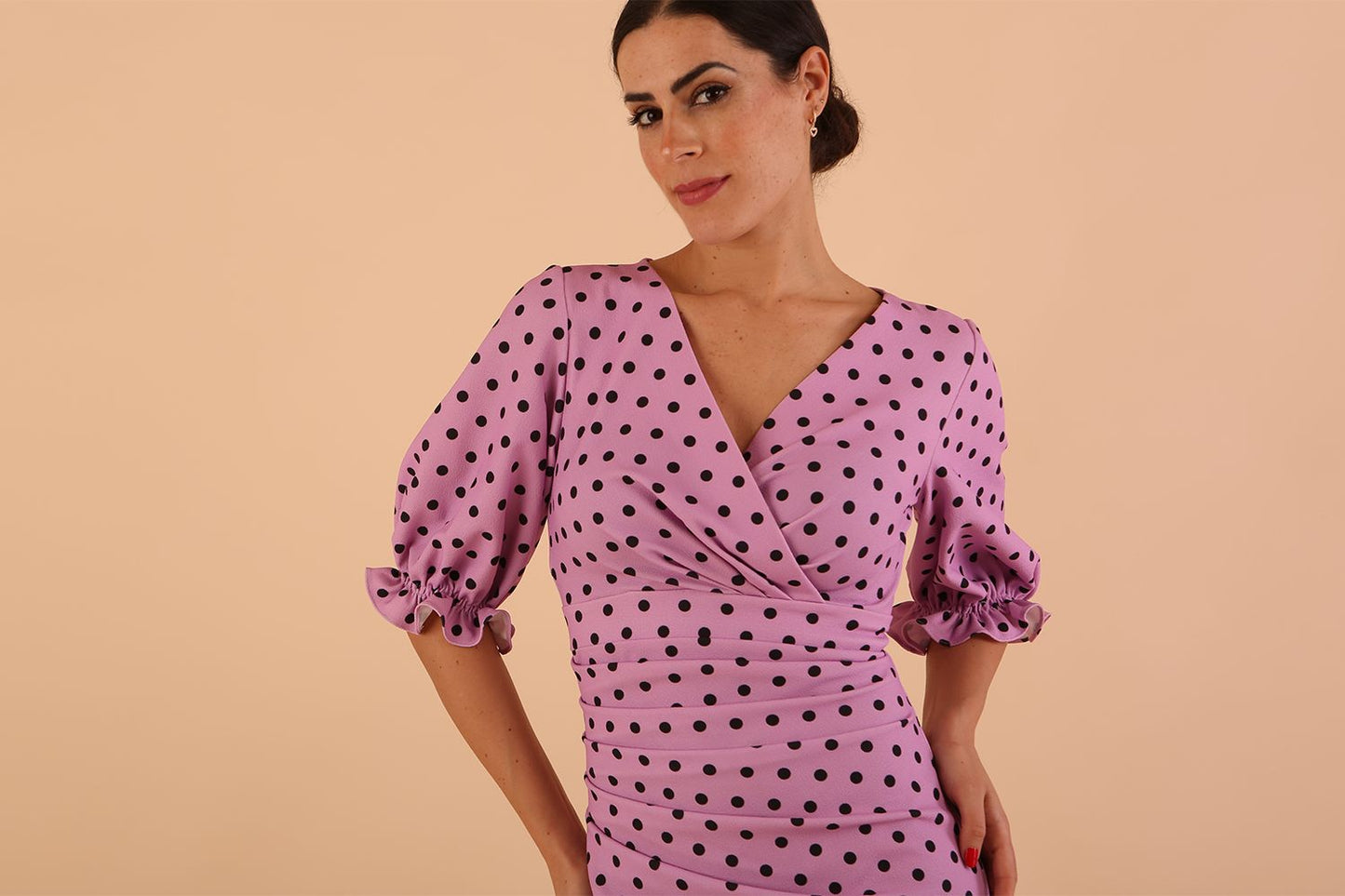 brunette model wearing diva catwalk palacio pencil fitted dress with three quarter puffed sleeve and pleating across the body with overlapping v-neckline in pink polka dot front