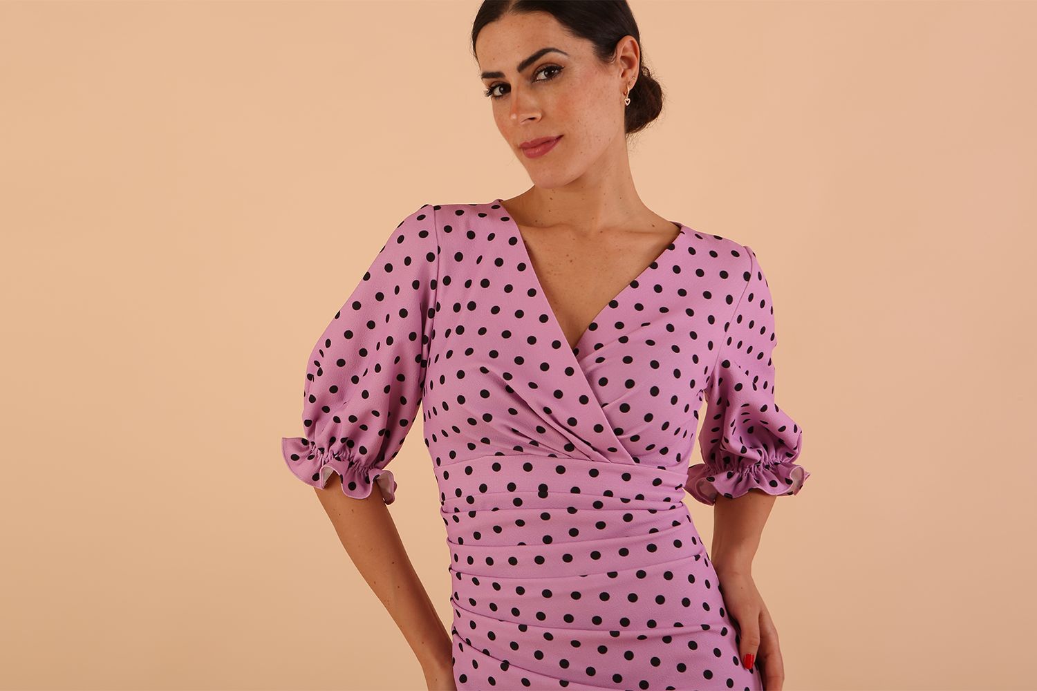 brunette model wearing diva catwalk palacio pencil fitted dress with three quarter puffed sleeve and pleating across the body with overlapping v-neckline in pink polka dot front