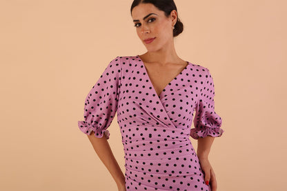 brunette model wearing diva catwalk palacio pencil fitted dress with three quarter puffed sleeve and pleating across the body with overlapping v-neckline in pink polka dot front