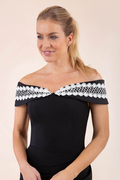 brunette model wearing diva catwalk kurumba pencil dress with bardot off shoulder neckline and lace detail across it in black and white colour front