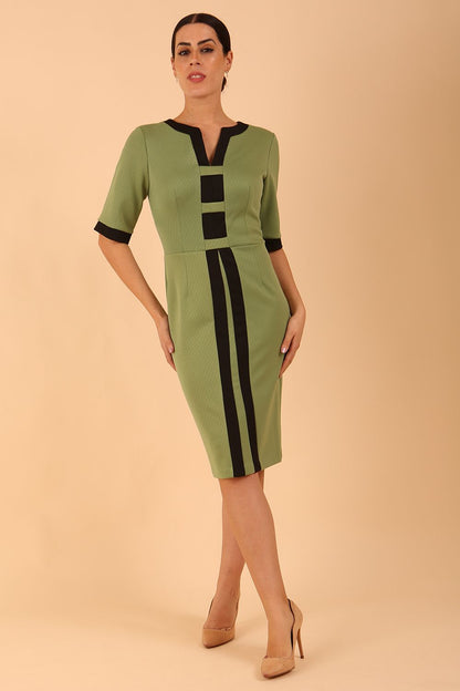 brunette model wearing Diva catwalk goggle pencil dress with short sleeve and v-neckline with contrasted design across body in dill green front