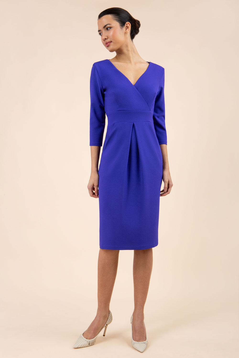 brunette model wearing diva catwalk wimpole a-line flattering dress with lowered v-neck and three quarter sleeve and cinching waistband and widened skirt with pleating in spectrum indigo front