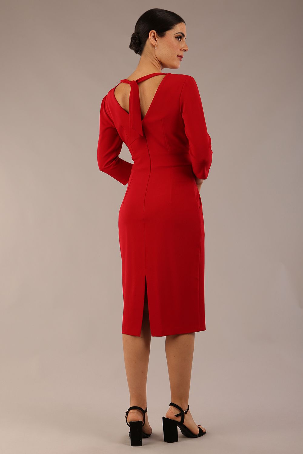 brunette model wearing diva catwalk wimpole a-line flattering dress with lowered v-neck and three quarter sleeve and cinching waistband and widened skirt with pleating in scarlet red front