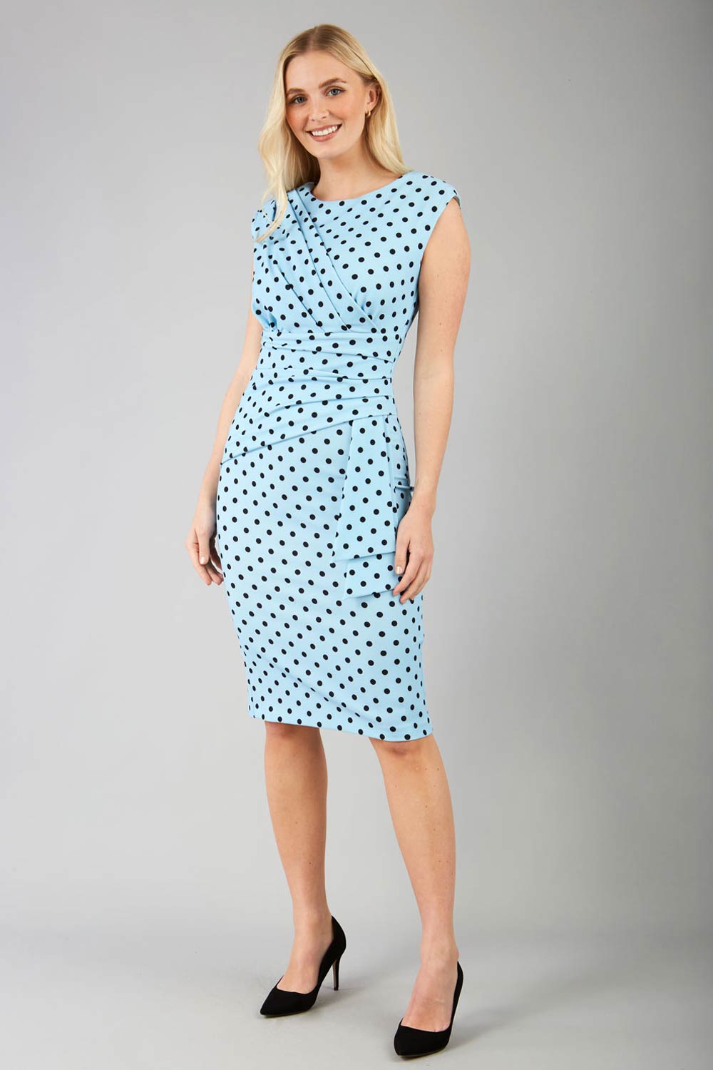 Brunette model wearing Diva Catwalk Perry Polka Dot Pencil Sleeveless Dress with tie detail on a side and rounded neckline in sky blue front