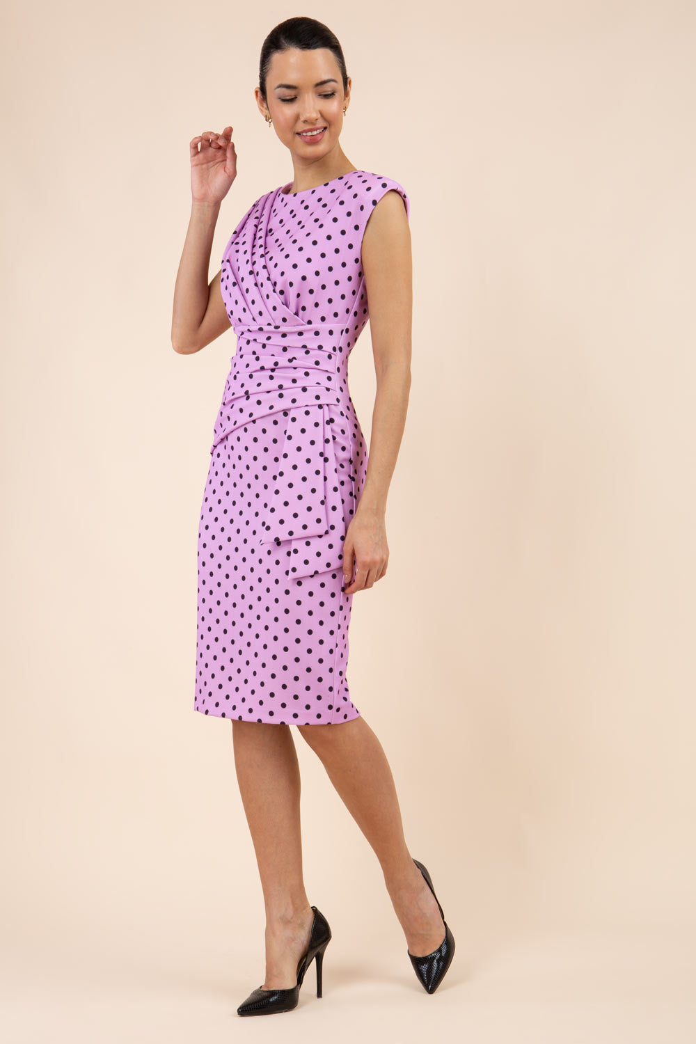 Brunette model wearing Diva Catwalk Perry Polka Dot Pencil Sleeveless Dress with tie detail on a side and rounded neckline in pink front