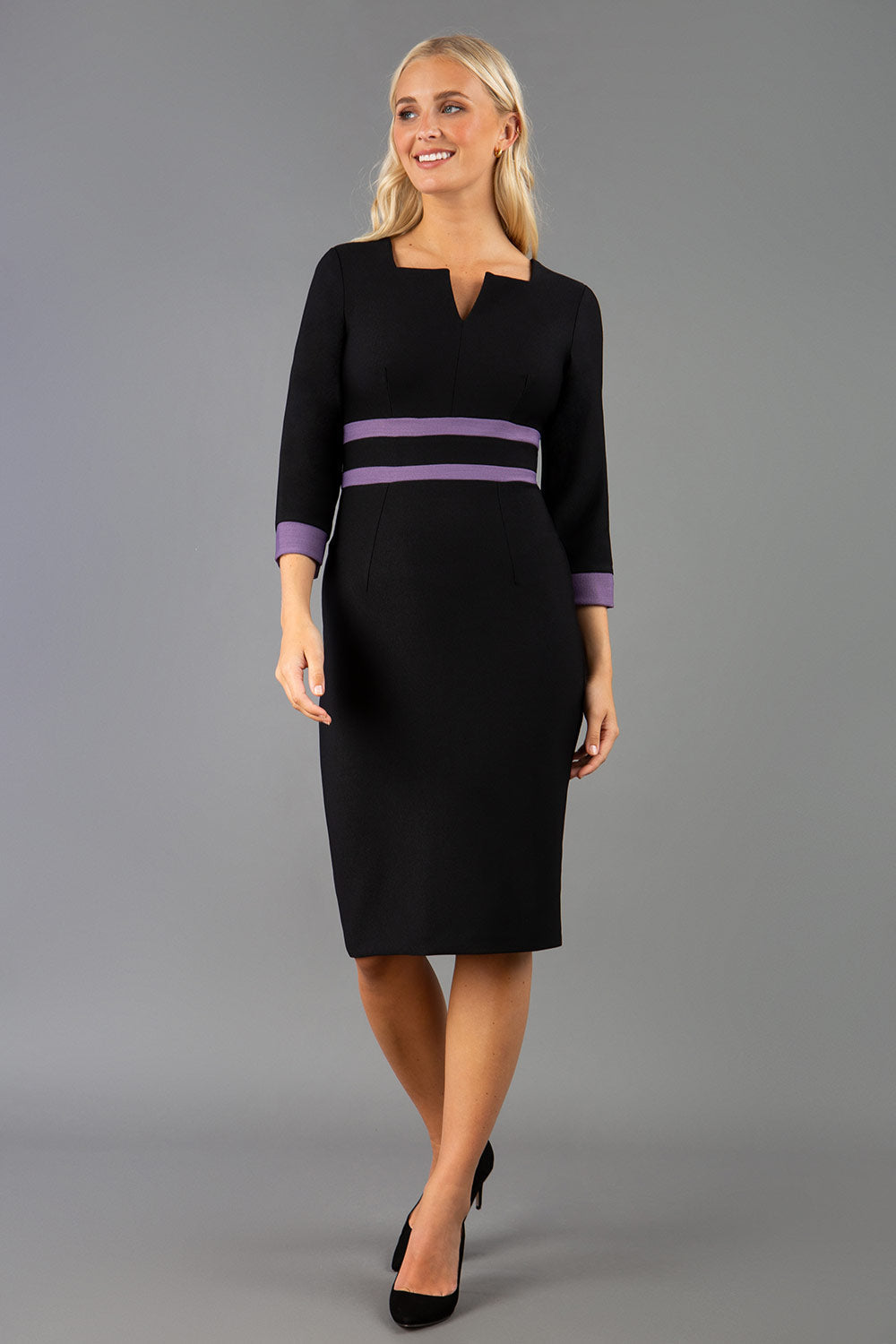 brunette model wearing Diva catwalk Paeonia dress square neckline with a vent in black with Dusky Lilac and black stripes around the waist and three quarter sleeve with Dusky Lilac contrast finish front