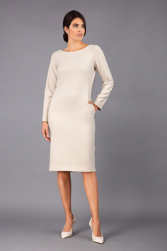 brunette model wearing diva catwalk cora white pencil dress with long sleeves and rounded neckline with pockets in colour sandy cream on side front