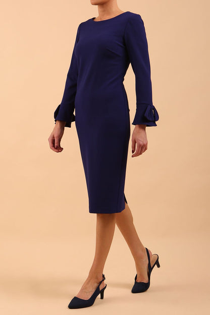 brunette model wearing diva catwalk fitted dress with sleeves called Alma Pencil-skirt dress in colour oxford blue with bow detail on sleeves front