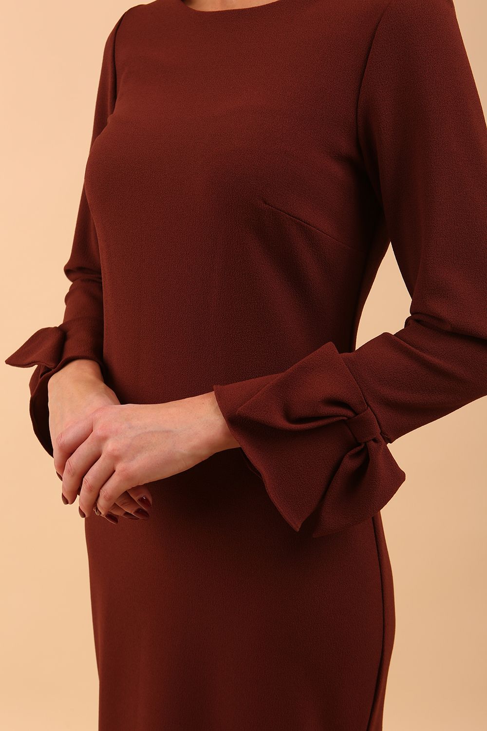 brunette model wearing diva catwalk fitted dress with sleeves called Alma Pencil-skirt dress in colour mahogany brown with bow detail on sleeves front