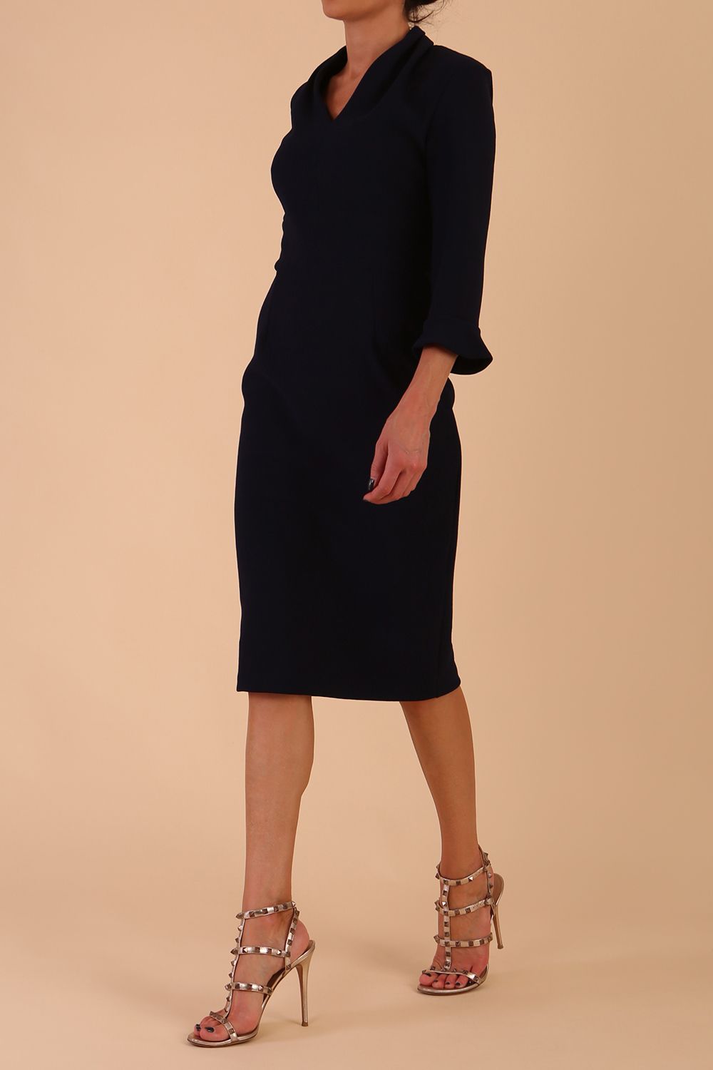 brunette model wearing diva catwalk adriana pencil dress with low v-neck and pleating around shoulders with three quarter sleeve detailed on end and wide waistband in dark navy front