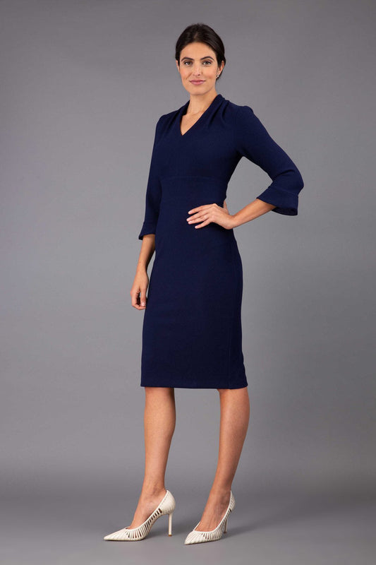 brunette model wearing diva catwalk adriana pencil dress with low v-neck and pleating around shoulders with three quarter sleeve detailed on end and wide waistband in dark navy front