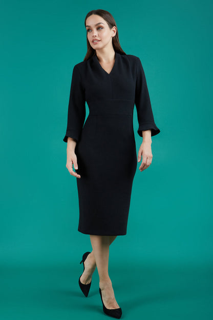 brunette model wearing diva catwalk adriana pencil dress with low v-neck and pleating around shoulders with three quarter sleeve detailed on end and wide waistband in black front