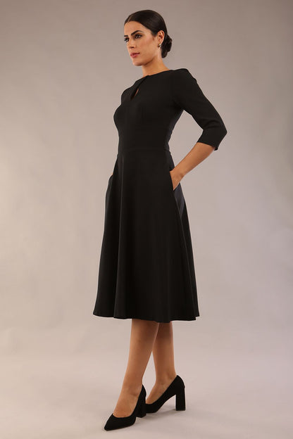 Brunette model is wearing diva catwalk casares swing dress with a keyhole neckline three quarter sleeve dress with pocket detail in black front (Black)