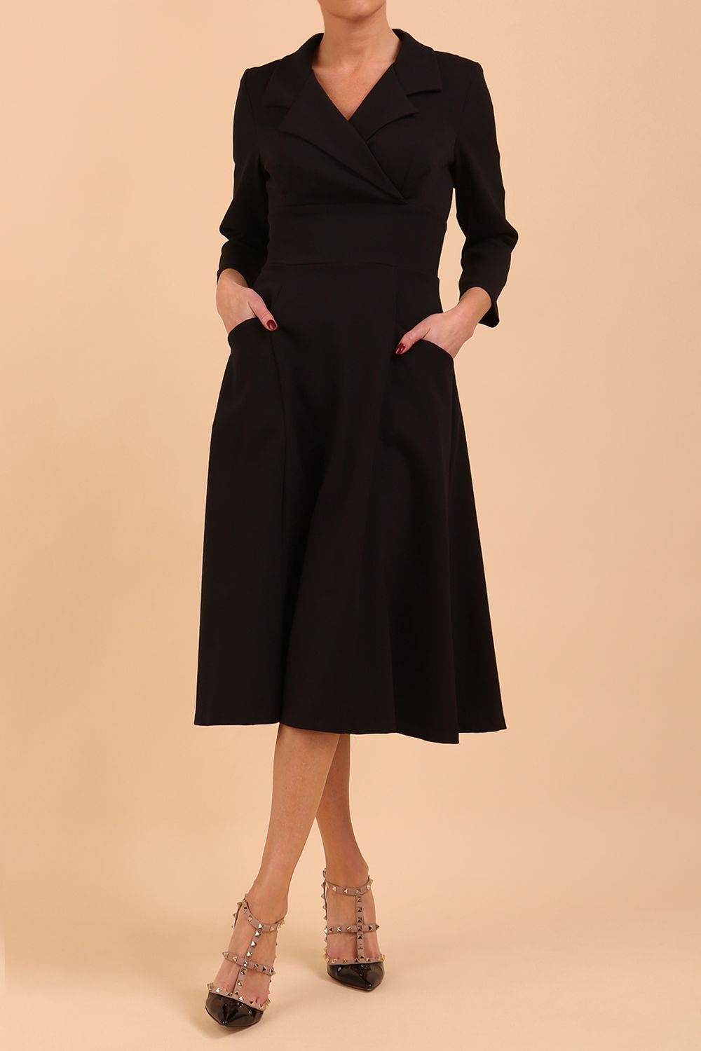 A blonde model is wearing a swing black three quarter sleeve dress with oversized collar and pockets in the skirt  
