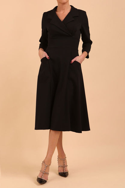 A blonde model is wearing a swing black three quarter sleeve dress with oversized collar and pockets in the skirt  