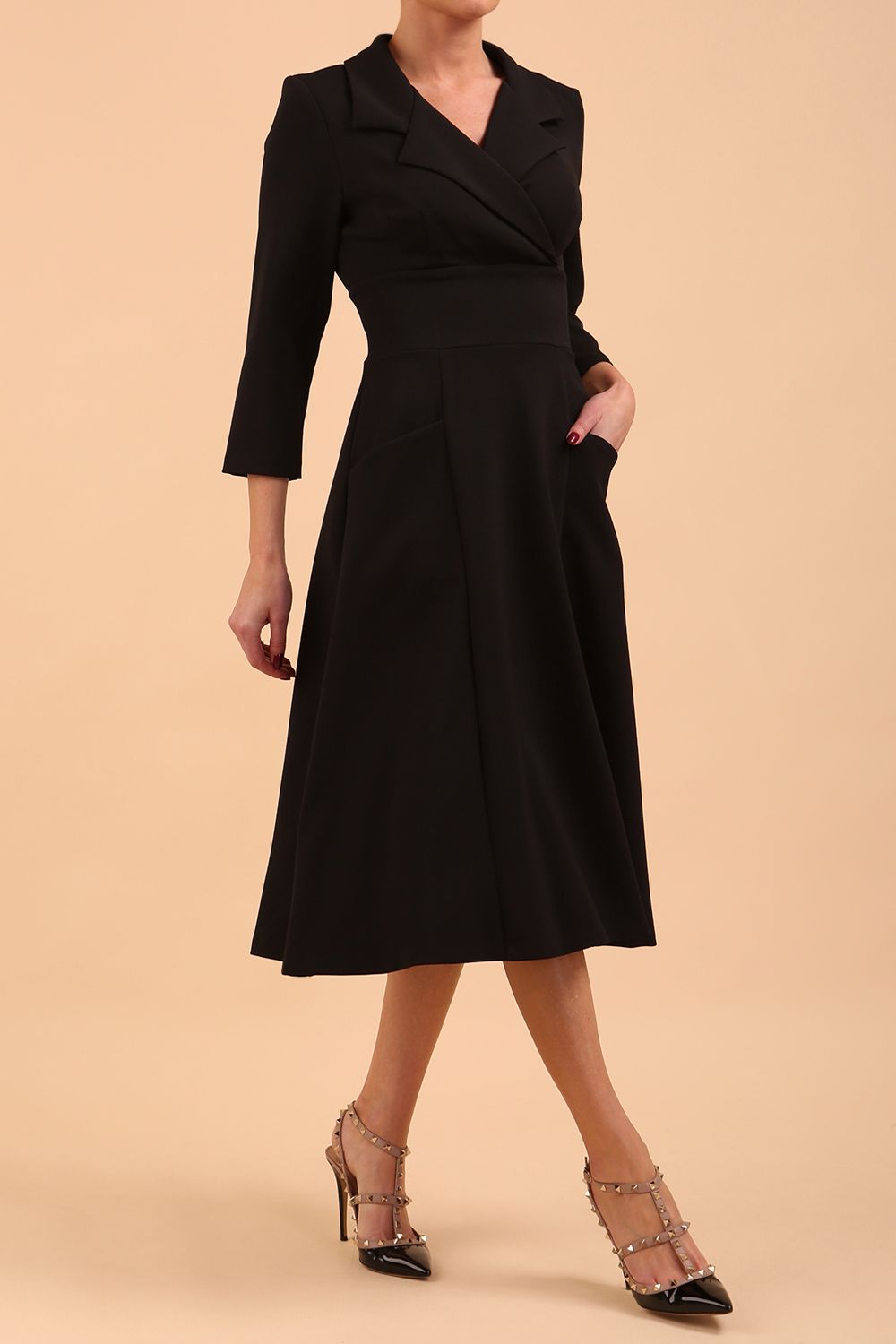 A blonde model is wearing a swing black three quarter sleeve dress with oversized collar and pockets in the skirt  