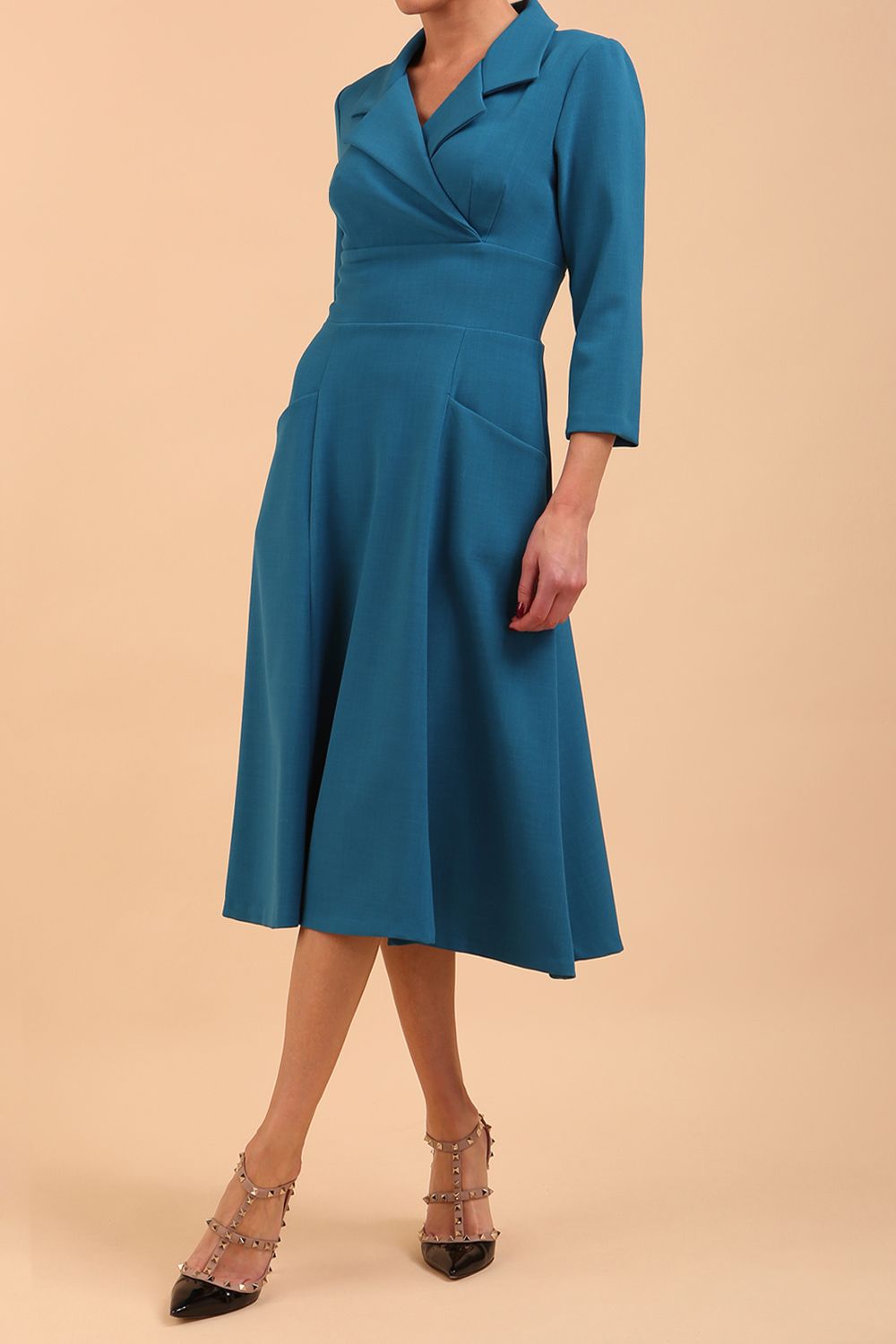 A brunette model is wearing a swing teal three quarter sleeve dress with oversized collar and pockets in the skirt