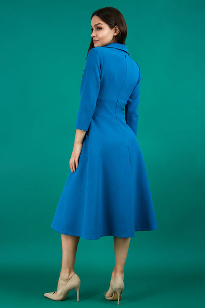 A brunette model is wearing a swing teal three quarter sleeve dress with oversized collar and pockets in the skirt
