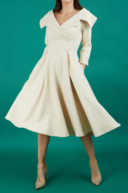 Brunette model is wearing a sleeved beige oversized collar swing dress with button detail at the front and pockets in the skirt