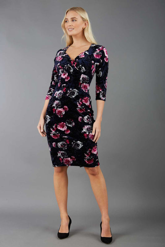 A blonde model is wearing a velvet pencil sweetheart neckline dress by diva catwalk in floral velvet print