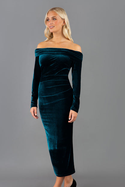A blonde Model is wearing an off shoulder bardot neckline velvet stretch midi  dress in teal green by diva catwalk back image
