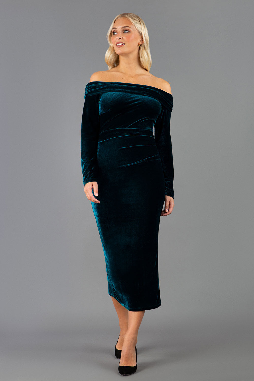 A blonde Model is wearing an off shoulder bardot neckline velvet stretch midi  dress in teal green by diva catwalk back image