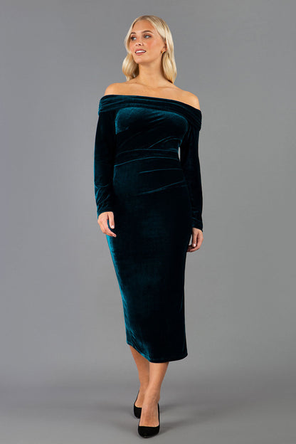 A blonde Model is wearing an off shoulder bardot neckline velvet stretch midi  dress in teal green by diva catwalk back image