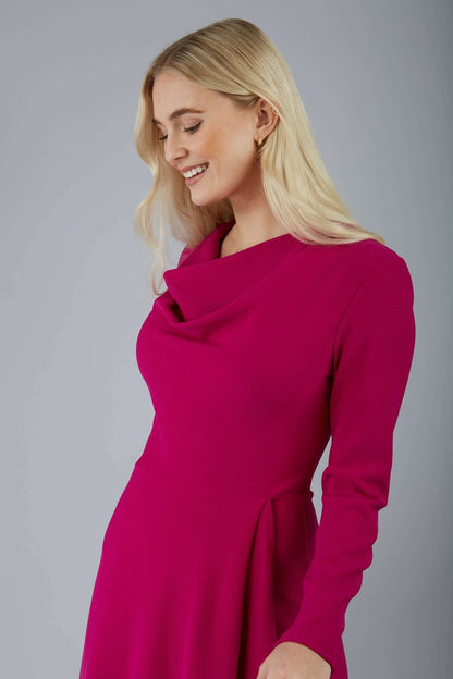 blonde model is wearing diva catwalk moraig swing long sleeve dress with high cowl neckline and wrap skirt in magenta front