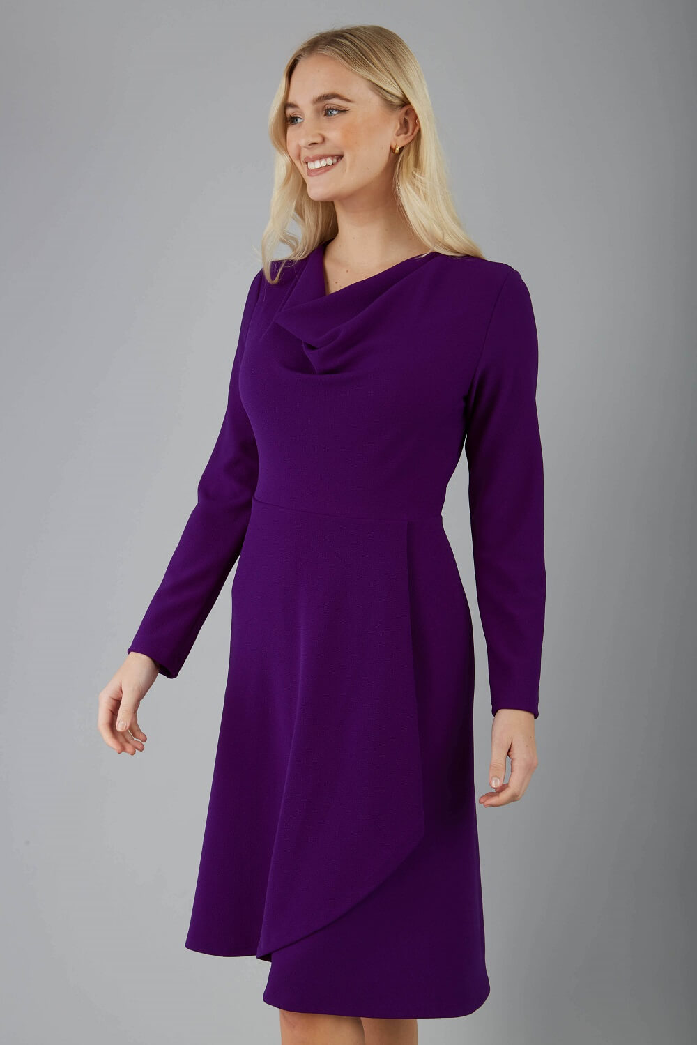 blonde model is wearing diva catwalk moraig swing long sleeve dress with high cowl neckline and wrap skirt in deep purple front
