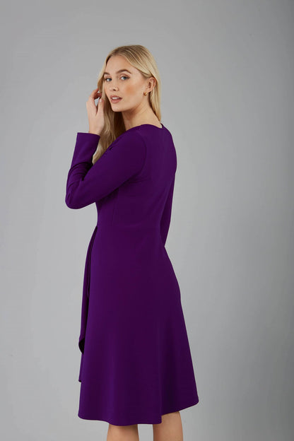 blonde model is wearing diva catwalk moraig swing long sleeve dress with high cowl neckline and wrap skirt in deep purple front