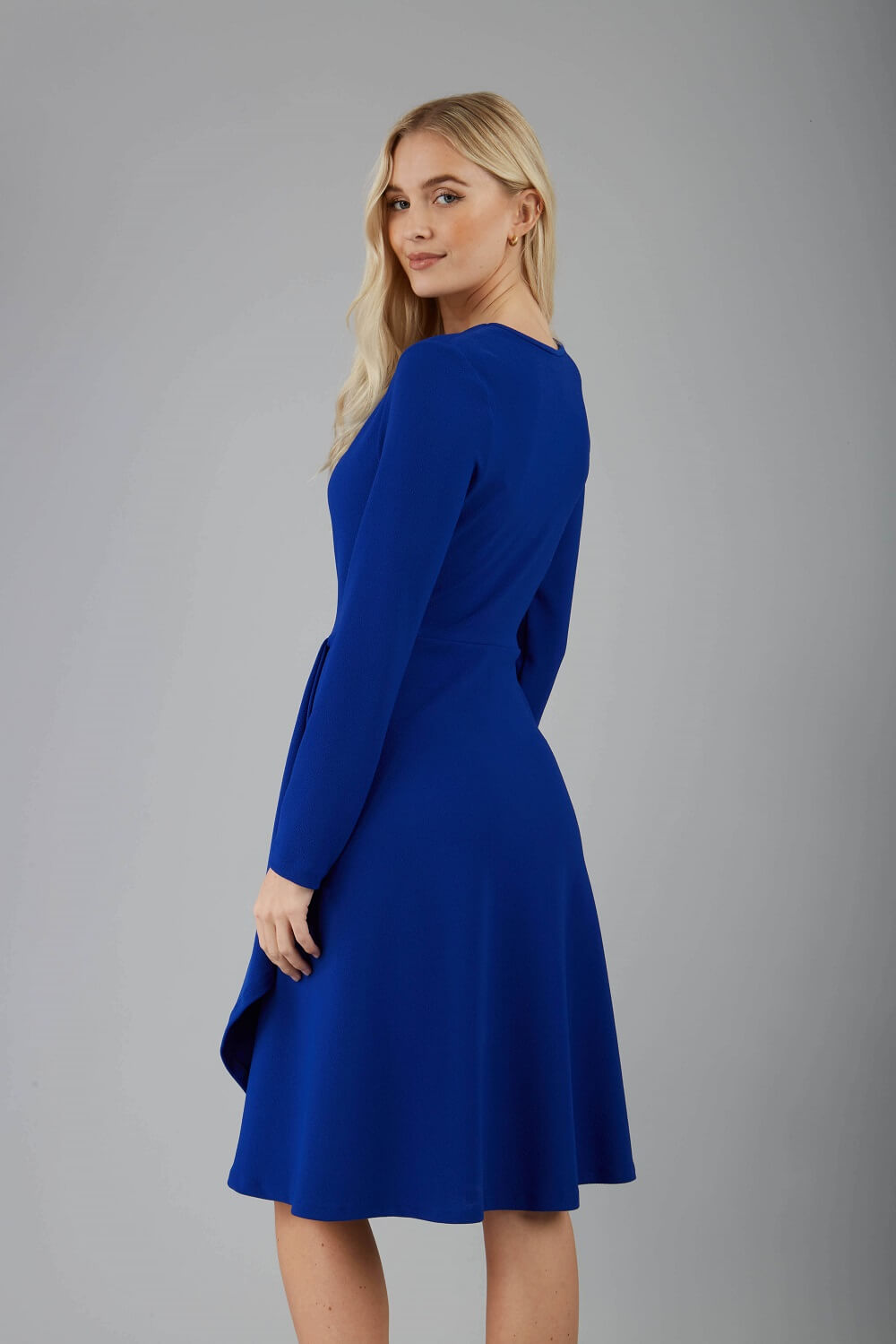 blonde model is wearing diva catwalk moraig swing long sleeve dress with high cowl neckline and wrap skirt in cobalt blue front