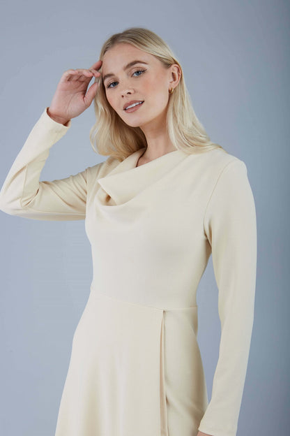 blonde model is wearing diva catwalk moraig swing long sleeve dress with high cowl neckline and wrap skirt in beige front