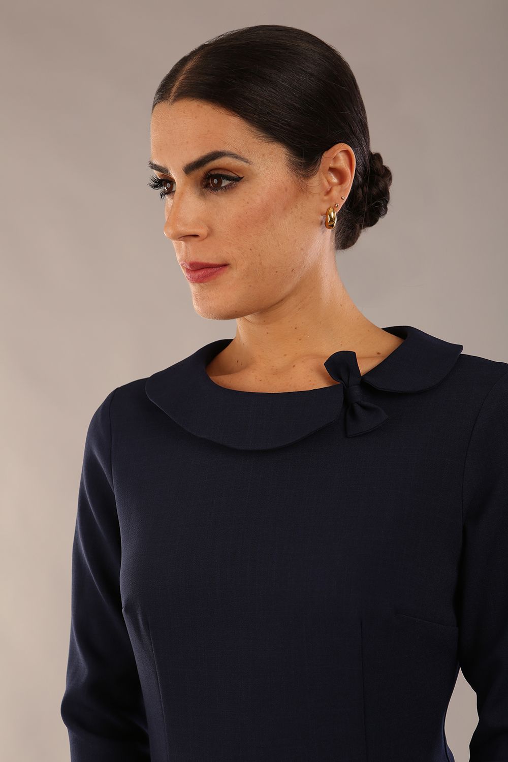 brunette model is wearing a diva catwalk  Helium 3/4 Sleeved Pencil Dress with 3/4 sleeve and knee length and bow detail on the neckline in navy blue colour front 