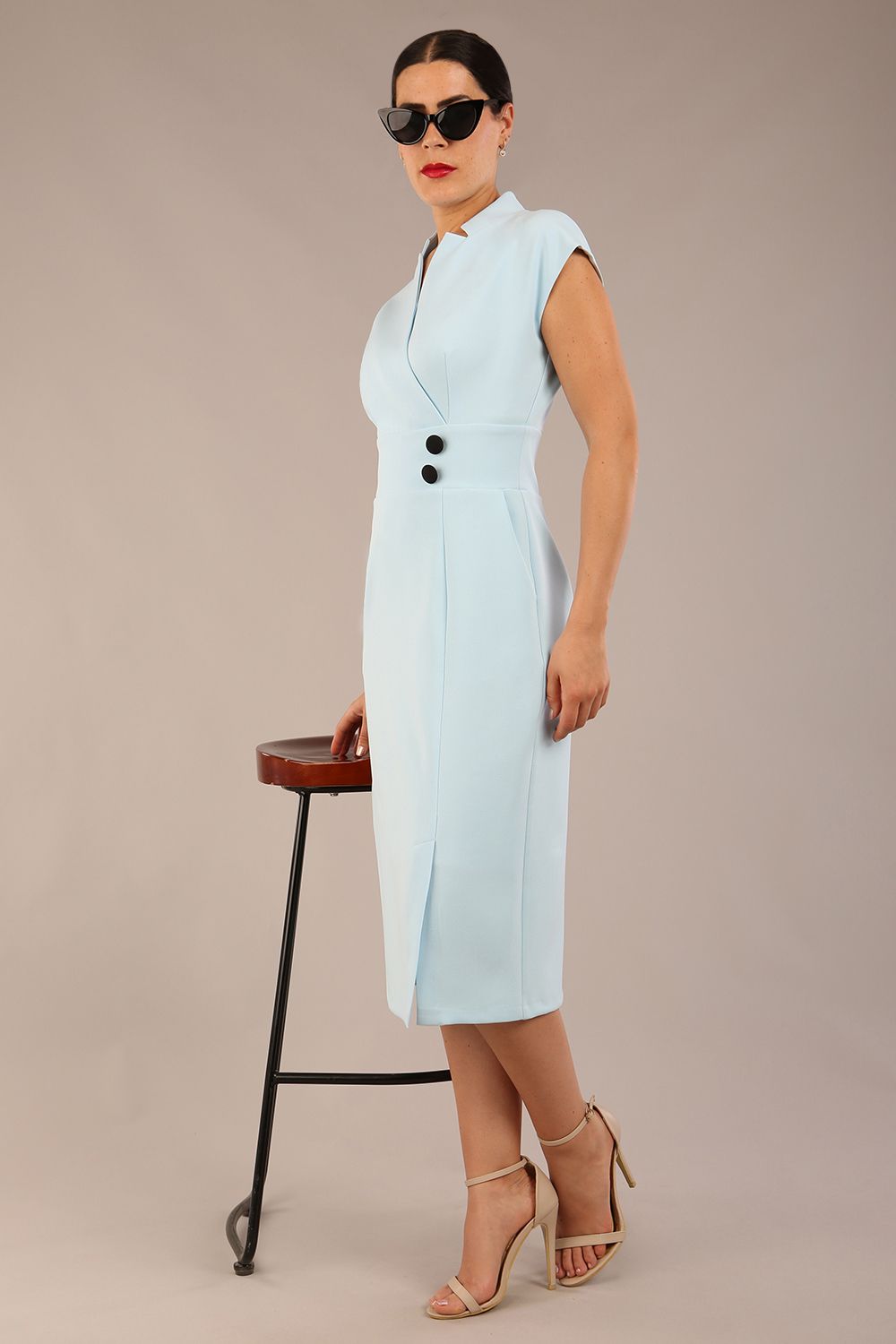 brunette Model is wearing a diva catwalk Derby pencil skirt dress cap sleeves with buttons details at the waistband and star neckline below the knee length with pockets in sky blue colour front image with sunglasses with a chair (Sky Blue)