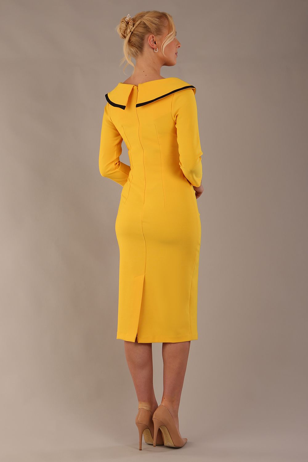 Model wearing diva catwalk Seed Elsye 3/4 Sleeve Knee Length Pencil Dress with Fold over bateau collar neckline with contrast piping and Bow feature on the left side of the bodice with decorative brooch in Daffodil Yellow colour front (Daffodil Yellow / Black Contrast)