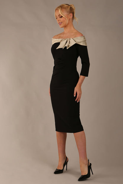 brunette Model is wearing a diva catwalk Rosalind Off Shoulder Bow Detail Pencil Dress 3/4 sleeve in Black/Champagne contrast front image (Black / Champagne Contrast)
