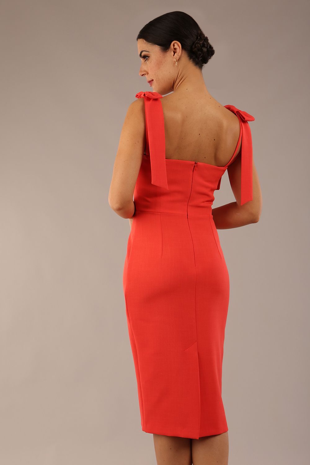 brunette model wearing a diva catwalk Philippa Pencil Wiggle Dress sleeveless style, tie detail on the shoulders knee length and sweetheart neckline in grenadine orange colour front