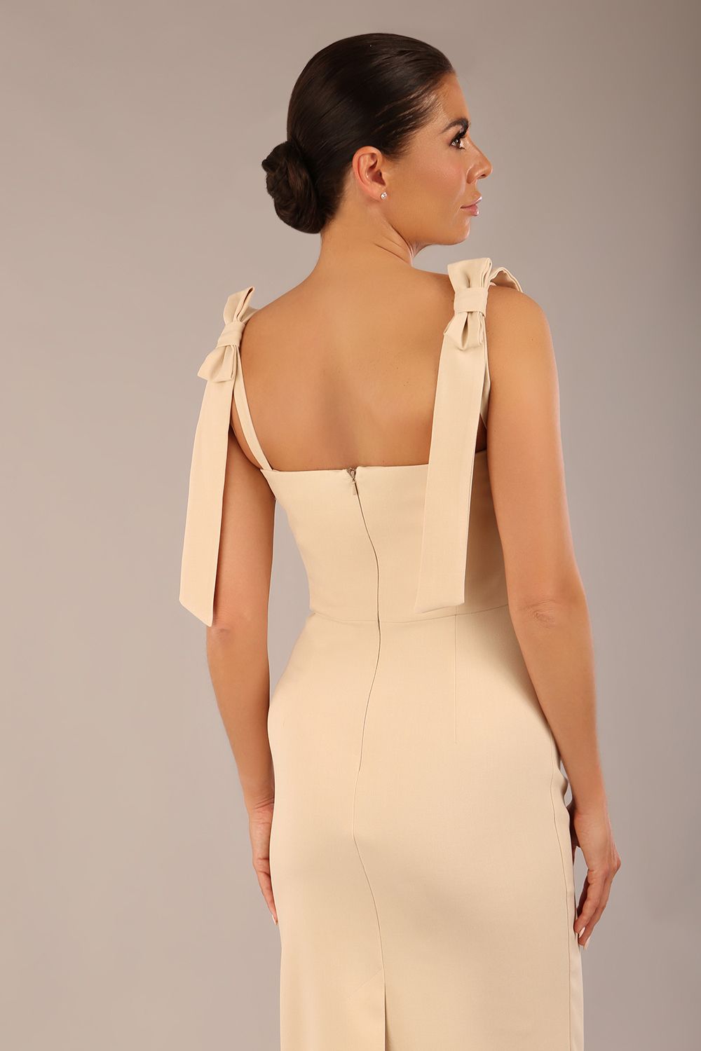 brunette model wearing a diva catwalk Philippa Pencil Wiggle Dress sleeveless style, tie detail on the shoulders knee length and sweetheart neckline in sandshell beige  front