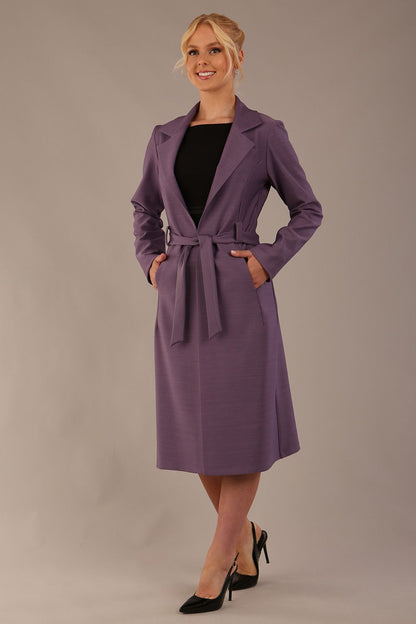 Model wearing a diva catwalk Paloma midi coat worn open over a black dress to show its versatility against a plain background (Dusky Lilac)