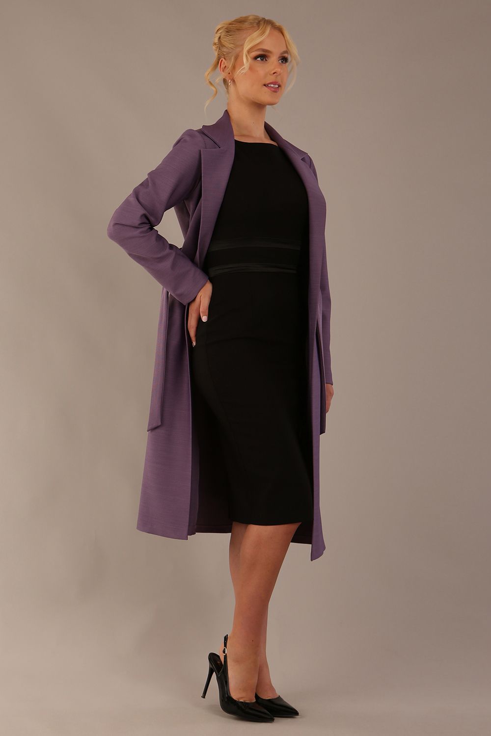 Model wearing a diva catwalk Paloma midi coat worn open over a black dress to show its versatility against a plain background (Dusky Lilac)