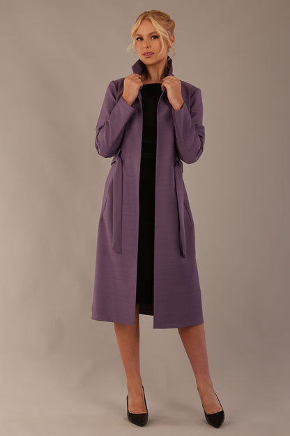 Model wearing a diva catwalk Paloma midi coat worn open over a black dress to show its versatility against a plain background (Dusky Lilac)