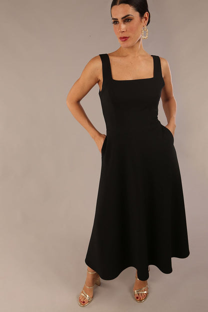 brunette model wearing a diva catwalk Tamsin Square Neckline Swing Dress sleeveless style with a midaxi  length and side pockets in Black colour front (Black)