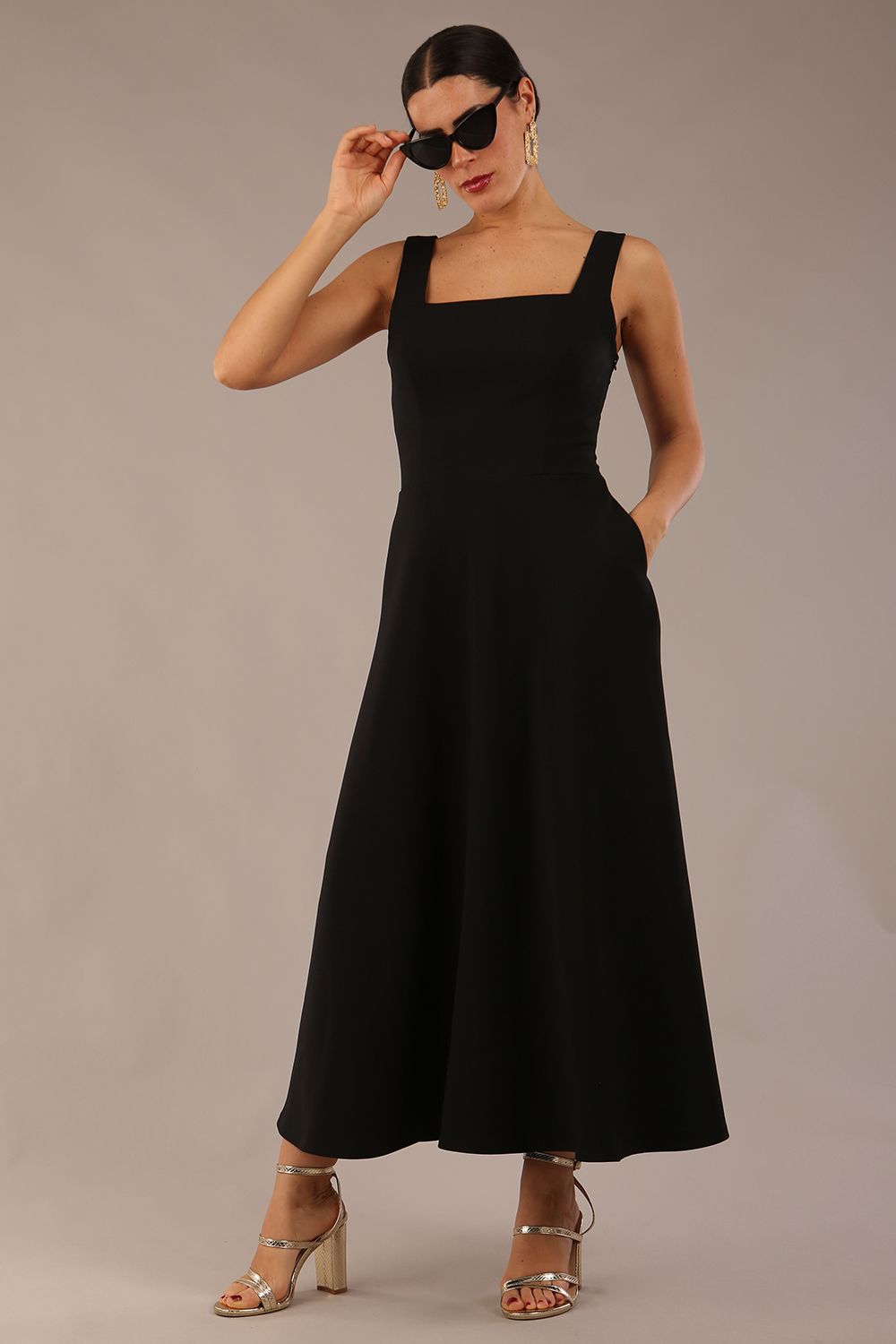 brunette model wearing a diva catwalk Tamsin Square Neckline Swing Dress sleeveless style with a midaxi  length and side pockets in Black colour front (Black)